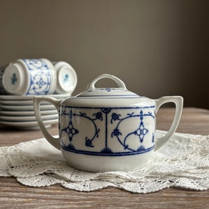 Peut inclure: Un sucrier en porcelaine blanche avec un motif floral bleu et blanc. Le bol a un couvercle et une poignée.
