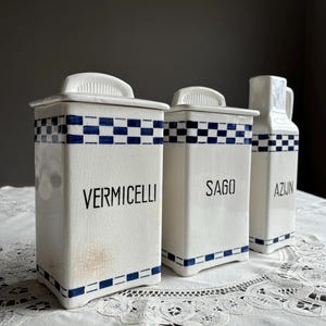 Può includere: Tre barattoli di ceramica bianca con disegni a scacchi blu e bianchi. I barattoli sono etichettati "Vermicelli", "Sago" e "Azun".