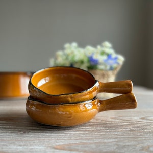 May include: Two brown ceramic ramekins with handles. The ramekins are stacked on top of each other.