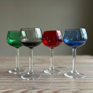 Op de afbeelding: Vier wijnglazen met steel en verschillende gekleurde glazen lichamen. De glazen zijn groen, zwart, rood en blauw.