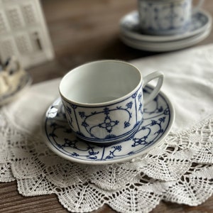 May include: A white teacup and saucer with a blue and white floral pattern. The saucer has a scalloped edge.