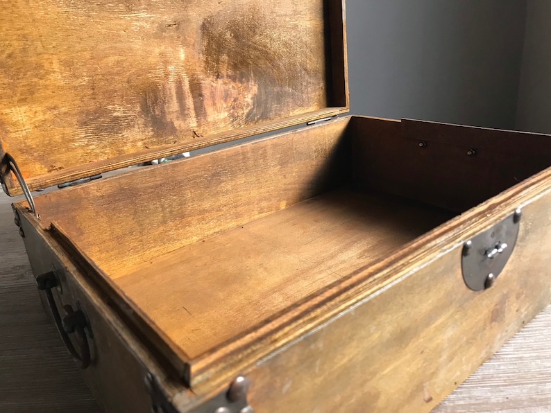 Puede incluir: Una caja de madera vac&iacute;a con una tapa con bisagras y detalles met&aacute;licos. La caja est&aacute; hecha de madera marr&oacute;n claro y tiene un acabado natural. La caja est&aacute; abierta y el interior es visible.