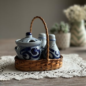 May include: A set of three blue and white ceramic salt and pepper shakers and a sugar bowl with a lid, all in a woven wicker basket with a handle.