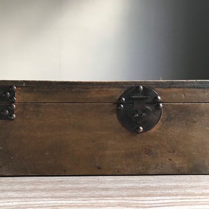 Puede incluir: Una caja de madera con tapa abatible y cierre de metal. La caja es marr&oacute;n y tiene un aspecto r&uacute;stico.