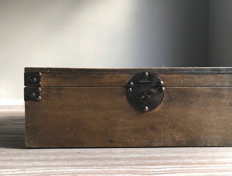 Puede incluir: Una caja de madera con tapa abatible y cierre de metal. La caja es marr&oacute;n y tiene un aspecto r&uacute;stico.