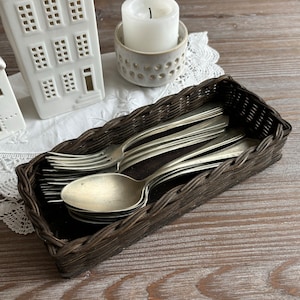 Puede incluir: Una cesta de mimbre marrón llena de cucharas y tenedores de plata. La cesta está sobre una mesa de madera.