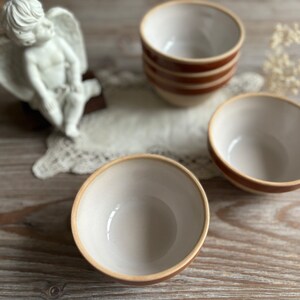 May include: Three white ceramic bowls with brown stripes. The bowls are on a wooden surface.