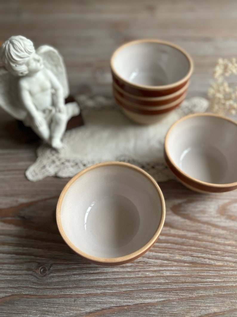 May include: Three white ceramic bowls with brown stripes. The bowls are on a wooden surface.