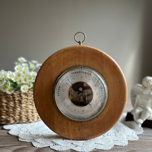 May include: A vintage wooden barometer with a silver face and a brass ring. The face reads "VERANDERLYK" and has markings for "STORM" and "BESTENDIG".