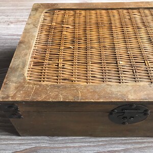 Puede incluir: Una caja de madera con una tapa de mimbre tejido. La caja tiene un cierre y bisagras de metal negro.