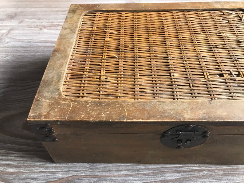 Puede incluir: Una caja de madera con una tapa de mimbre tejido. La caja tiene un cierre y bisagras de metal negro.