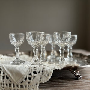 Könnte beinhalten: Ein Set aus sechs klaren Schnapsgläsern aus Glas mit geschliffenem Glasdesign. Die Gläser sind auf einem silbernen Tablett mit einer Spitzenunterlage angeordnet.