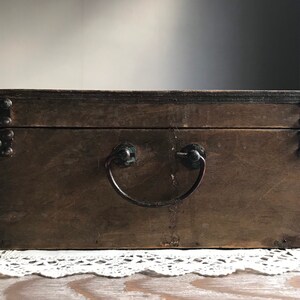 Puede incluir: Una caja de madera con una manija de metal y detalles met&aacute;licos. La caja es marr&oacute;n y tiene un aspecto desgastado.