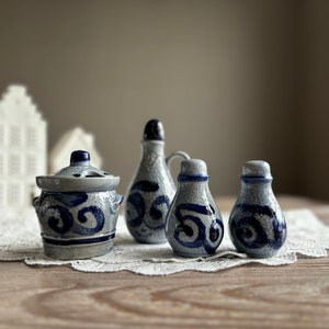 May include: Four ceramic salt and pepper shakers with blue and white designs. The shakers are in the shape of a bottle, a jar, and two small round containers. The shakers are on a white lace tablecloth.