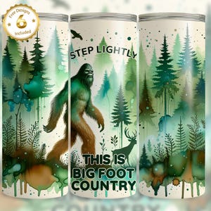 Puede incluir: Un vaso cilíndrico con un tema de Bigfoot. El diseño presenta una ilustración de acuarela de Bigfoot caminando por un bosque con pinos y el texto "Step Lightly, This is Big Foot Country". Incluye un sello dorado que dice "Free Designs 6 Included".