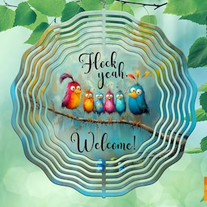 Könnte beinhalten: Ein dekorativer Windspinner aus Metall mit einem mehrschichtigen Design, das eine Cartoon-Vogelgruppe auf einem Ast zeigt. Der Text "Flock yeah. Welcome!" ist abgebildet. Geeignet für Gärten.