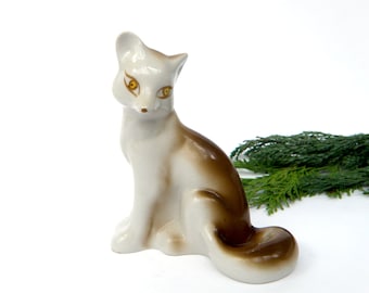 May include: A white porcelain figurine of a fox sitting with its tail curled around its body. The fox has brown markings on its back and tail, and yellow eyes.