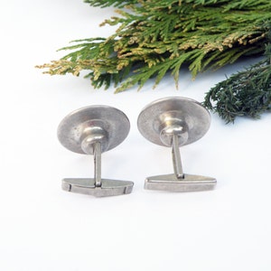 May include: A pair of silver cufflinks with a round, slightly domed design. The cufflinks have a simple, classic style.