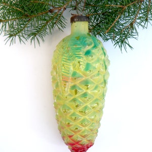 May include: A vintage Christmas ornament shaped like a pine cone, with a textured surface and a gradient of colors. The ornament transitions from yellow-green to red at the base. A sprig of evergreen needles is in the background.