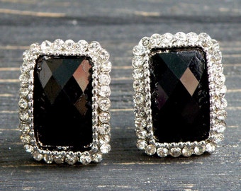 May include: A pair of silver earrings with black rectangular stones surrounded by clear rhinestones.