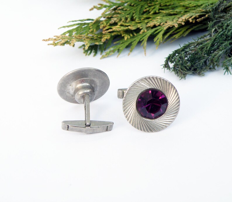 May include: A pair of silver cufflinks with a purple gemstone in the center of one cufflink.