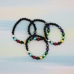 May include: Four black beaded bracelets with colorful beads. The bracelets are layered on top of each other.