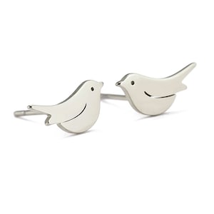 May include: A pair of silver bird stud earrings. Each earring features a simple, minimalist design of a bird with a small, round head and a slightly curved body.