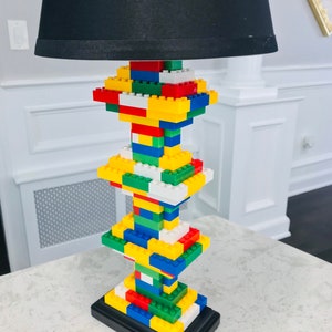 Op de afbeelding: Een zwarte lampenkap met een basis van kleurrijke Lego-stenen.