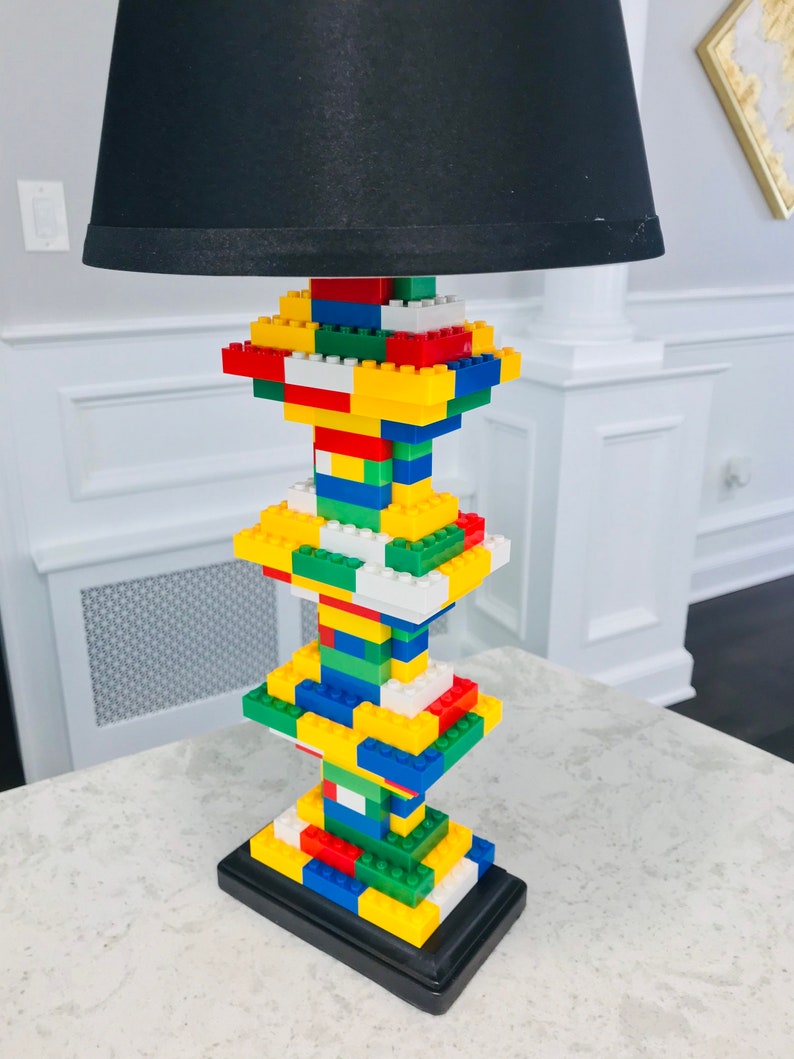 Op de afbeelding: Een zwarte lampenkap met een basis van kleurrijke Lego-stenen.