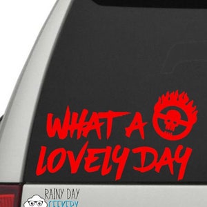 Puede incluir: Pegatina de vinilo roja para un coche con el texto "What a lovely day" y un diseño estilizado de calavera y llamas.