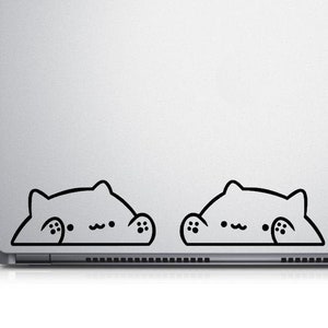 May include: A silver laptop with two black cat stickers on the bottom edge of the screen. The stickers are of a cartoon cat with a surprised expression, peeking over the edge of the screen.