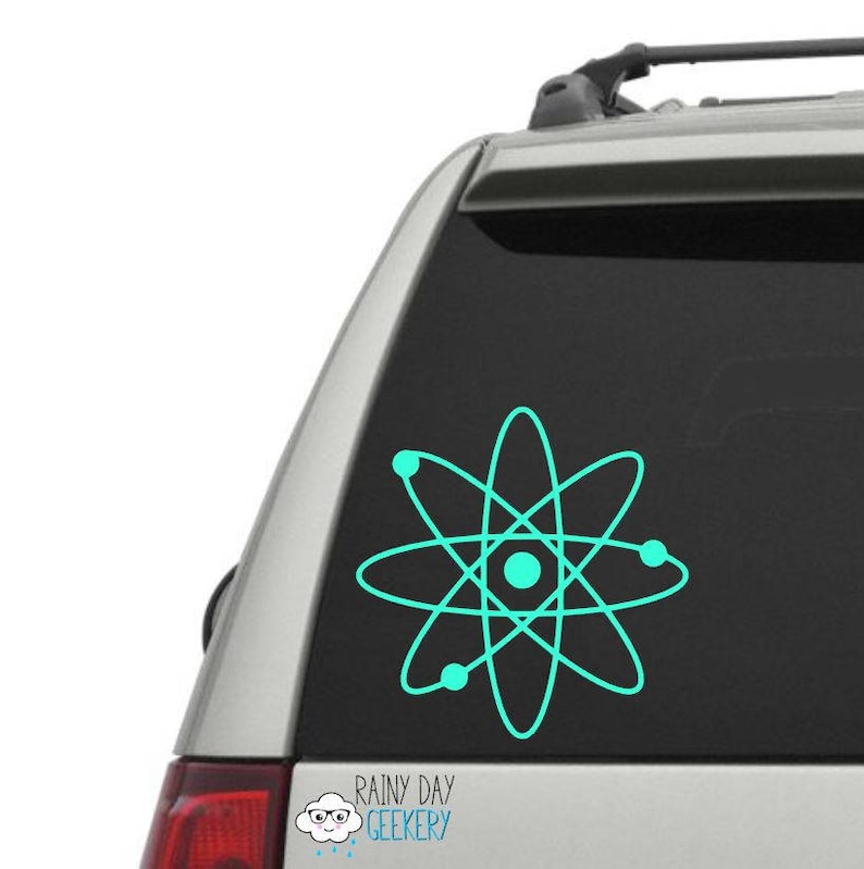 May include: A teal blue atom symbol decal on a silver car. The decal is a simple design with a circle in the center and five orbiting electrons.