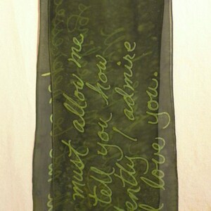 Puede incluir: Una bufanda de seda verde oscuro con una inscripci&oacute;n en verde claro que dice "Debes permitirme decirte cu&aacute;nto te admiro y te amo."