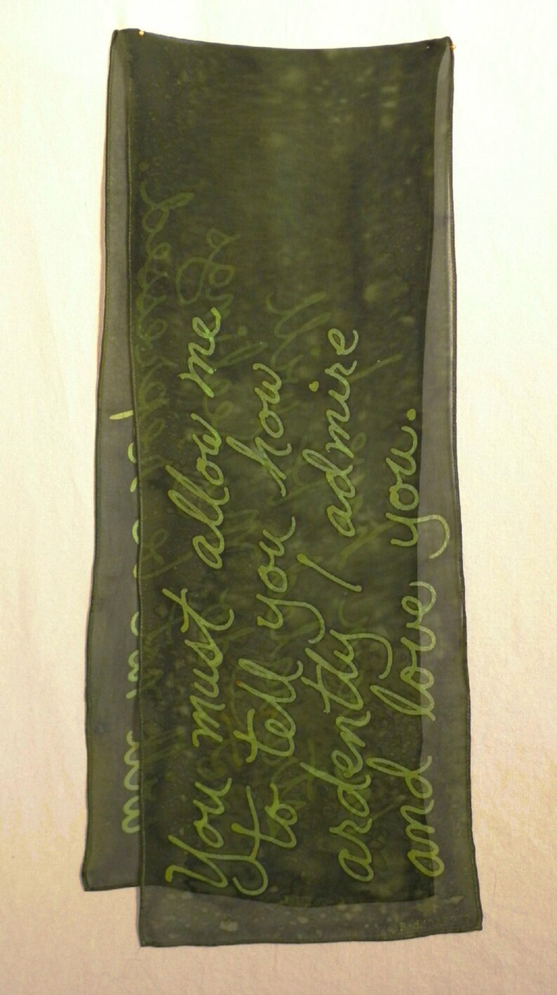 Puede incluir: Una bufanda de seda verde oscuro con una inscripci&oacute;n en verde claro que dice "Debes permitirme decirte cu&aacute;nto te admiro y te amo."