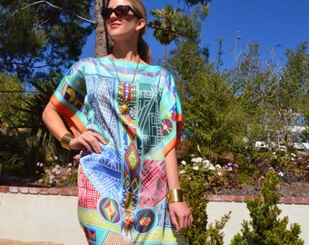 Puede incluir: Una mujer lleva un vestido colorido con estampado geométrico y detalles dorados. El vestido tiene una silueta suelta y fluida y un escote redondo. Lleva gafas de sol y un collar de oro.