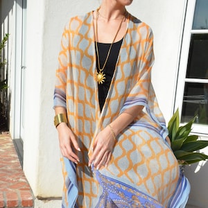 May include: A sheer, lightweight kimono with a geometric pattern in shades of blue and yellow. The kimono has a blue and gold paisley border. The model is wearing the kimono over a black tank top and black leggings.