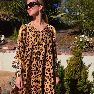 May include: A brown and black leopard print kaftan with gold accents and a gold chain necklace with a sun pendant.
