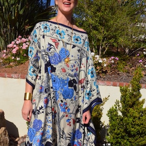 K&ouml;nnte beinhalten: Ein wei&szlig;es Maxikleid mit einem blauen, roten und schwarzen Blumendruck. Das Kleid hat einen quadratischen Ausschnitt und eine flie&szlig;ende Silhouette. Das Kleid ist aus einem leichten Stoff gefertigt und perfekt f&uuml;r warmes Wetter.