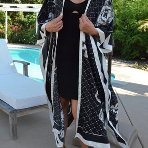 May include: A black and white patterned kimono with a white trim. The kimono is worn over a black dress. The person is wearing brown sandals.