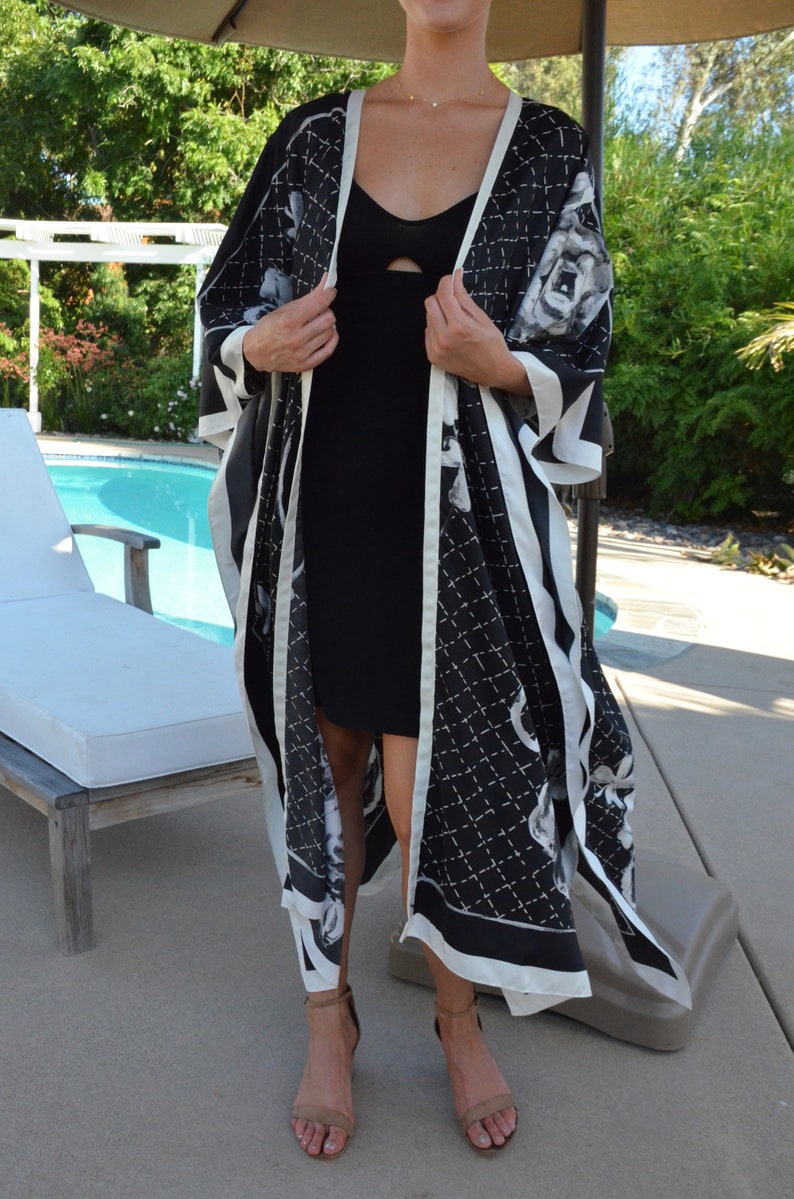 May include: A black and white patterned kimono with a white trim. The kimono is worn over a black dress. The person is wearing brown sandals.
