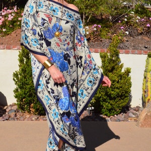 K&ouml;nnte beinhalten: Eine Frau tr&auml;gt eine wei&szlig;e und blaue Kaftan mit floralem Muster, eine goldene Halskette und ein Armband. Die Kaftan hat einen quadratischen Ausschnitt und eine flie&szlig;ende Silhouette.