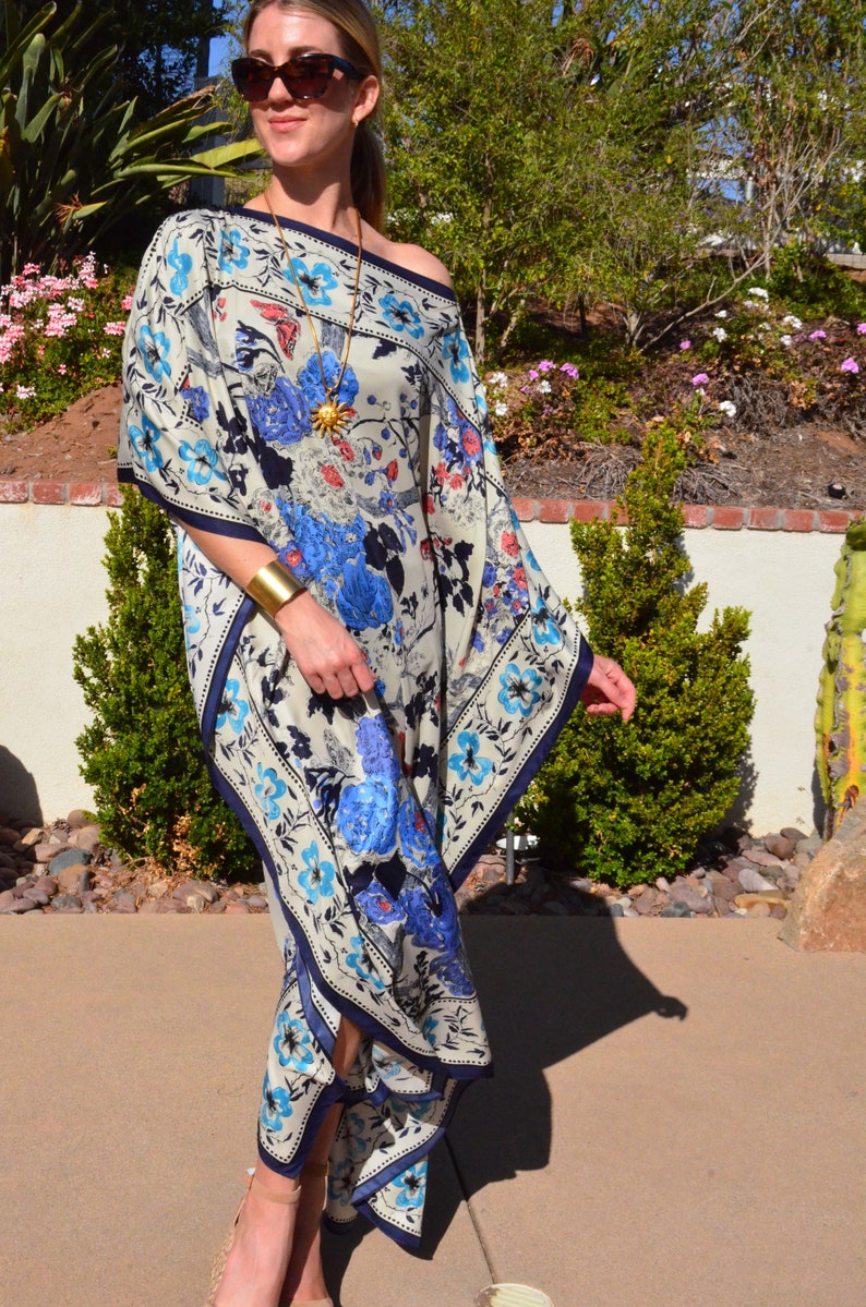 K&ouml;nnte beinhalten: Eine Frau tr&auml;gt eine wei&szlig;e und blaue Kaftan mit floralem Muster, eine goldene Halskette und ein Armband. Die Kaftan hat einen quadratischen Ausschnitt und eine flie&szlig;ende Silhouette.