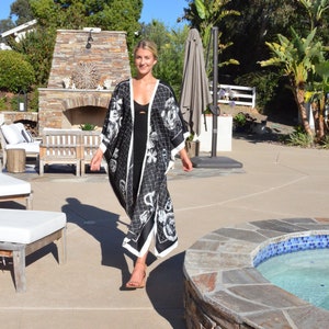 May include: A woman wearing a black and white floral kimono with a black tank top underneath. She is standing in a garden with a stone fireplace and a hot tub in the background.