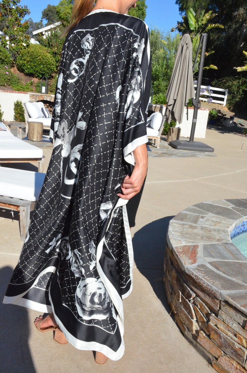 May include: A black and white kimono with a floral pattern and a quilted design. The kimono is being worn by a person standing in a garden setting.