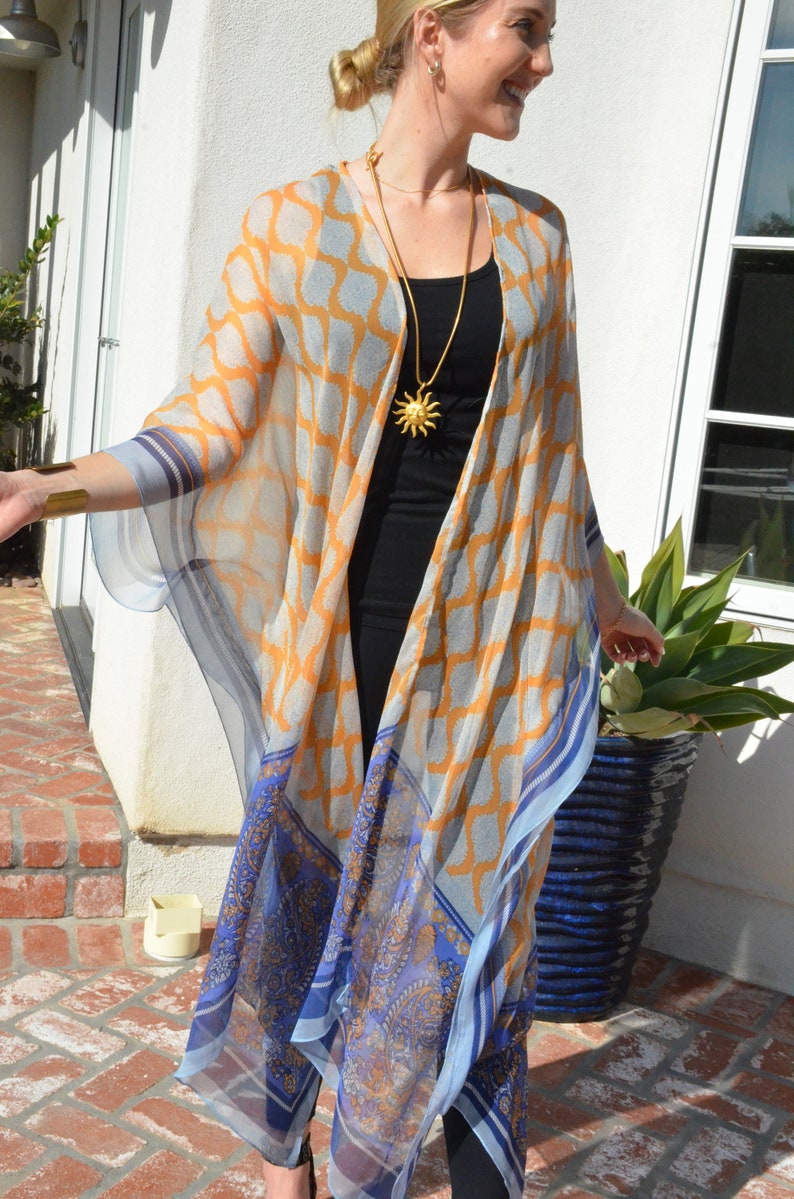 May include: A sheer, long, blue and orange patterned kimono with a gold sun pendant necklace.