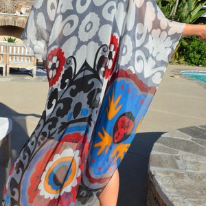 Op de afbeelding: Een doorschijnende, lichte kimono met een kleurrijk bloemenpatroon. De kimono is gemaakt van een zachte, vloeiende stof en heeft een verscheidenheid aan kleuren, waaronder rood, blauw, geel en wit.