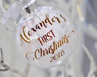 May include: Clear glass Christmas bauble with gold lettering that reads "Alexander's First Christmas 2018".