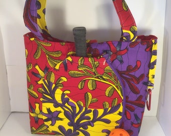 May include: A red, yellow, and purple patterned tote bag with a black racquet and an orange ball. The bag has a zipper closure and a long strap.