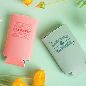 Op de afbeelding: Twee drankisolatoren, &eacute;&eacute;n koraal en &eacute;&eacute;n zeegroen, liggen op een lichtgroen oppervlak. Op de koraal isolator staat de tekst "BOOKS CAFFEINE BOOKS BOOKS". Op de zeegroene isolator staat de tekst "CAFFEINE & BOOKS".