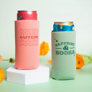 Op de afbeelding: Twee blikjeskoelers, &eacute;&eacute;n koraal en &eacute;&eacute;n mintgroen, elk met een blikje. De koraalkoeler heeft de tekst "BOOKS CAFFEINE BOOKS" in een retro lettertype. De mintgroene koeler heeft de tekst "CAFFEINE & BOOKS."